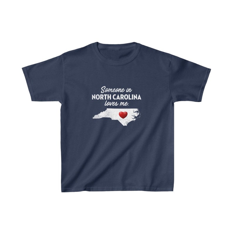 K&ouml;nnte beinhalten: Ein marineblaues T-Shirt mit einer wei&szlig;en Umrandung des Bundesstaates North Carolina und einem roten Herzen in der Mitte. Der Text "Someone in North Carolina loves me." ist auf das T-Shirt gedruckt.