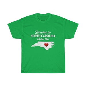 May include: Green t-shirt with a white outline of the state of North Carolina and a red heart in the center. The text "Someone in North Carolina loves me." is printed on the shirt.