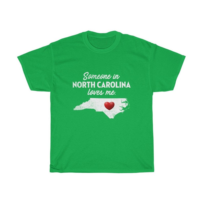May include: Green t-shirt with a white outline of the state of North Carolina and a red heart in the center. The text "Someone in North Carolina loves me." is printed on the shirt.