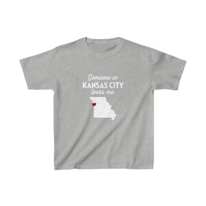 May include: Gray t-shirt with the text "Someone in KANSAS CITY loves me." and a white outline of the state of Missouri with a red heart over Kansas City.