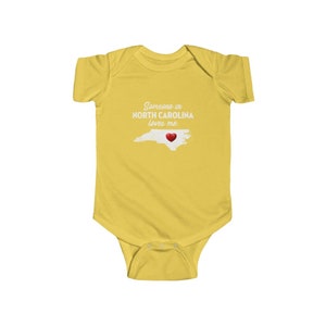 Peut inclure: Combinaison jaune pour b&eacute;b&eacute; avec le texte "Quelqu'un en Caroline du Nord m'aime." et un c&oelig;ur rouge sur un contour de l'&eacute;tat de Caroline du Nord.