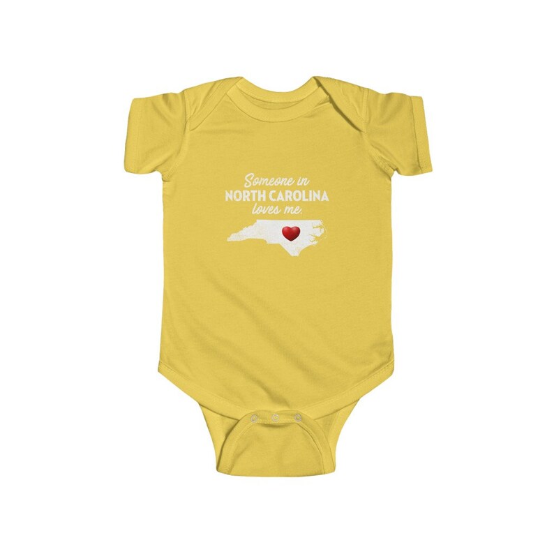 Peut inclure: Combinaison jaune pour b&eacute;b&eacute; avec le texte "Quelqu'un en Caroline du Nord m'aime." et un c&oelig;ur rouge sur un contour de l'&eacute;tat de Caroline du Nord.