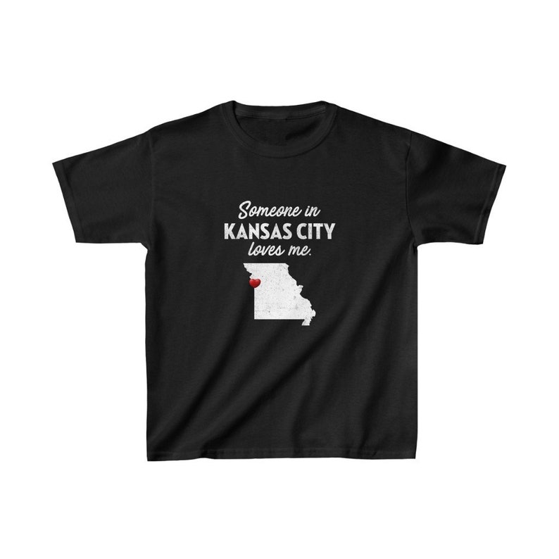 May include: Black t-shirt with white text that reads "Someone in Kansas City loves me." The text is centered on the shirt. A white outline of the state of Missouri is below the text with a red heart marking the location of Kansas City.