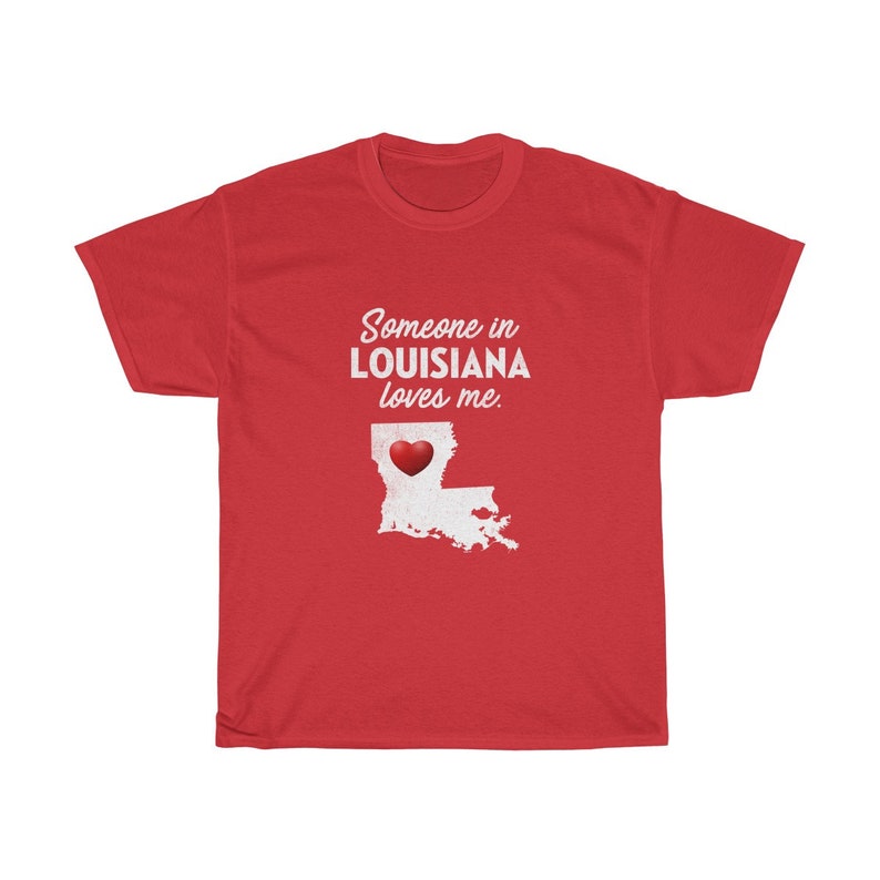 May include: Red t-shirt with white text that says "Someone in Louisiana loves me."  The text is over a white outline of the state of Louisiana with a red heart in the center.