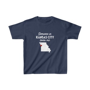 May include: Navy blue t-shirt with a white outline of the state of Missouri and the text "Someone in Kansas City loves me." A red heart is placed over Kansas City.