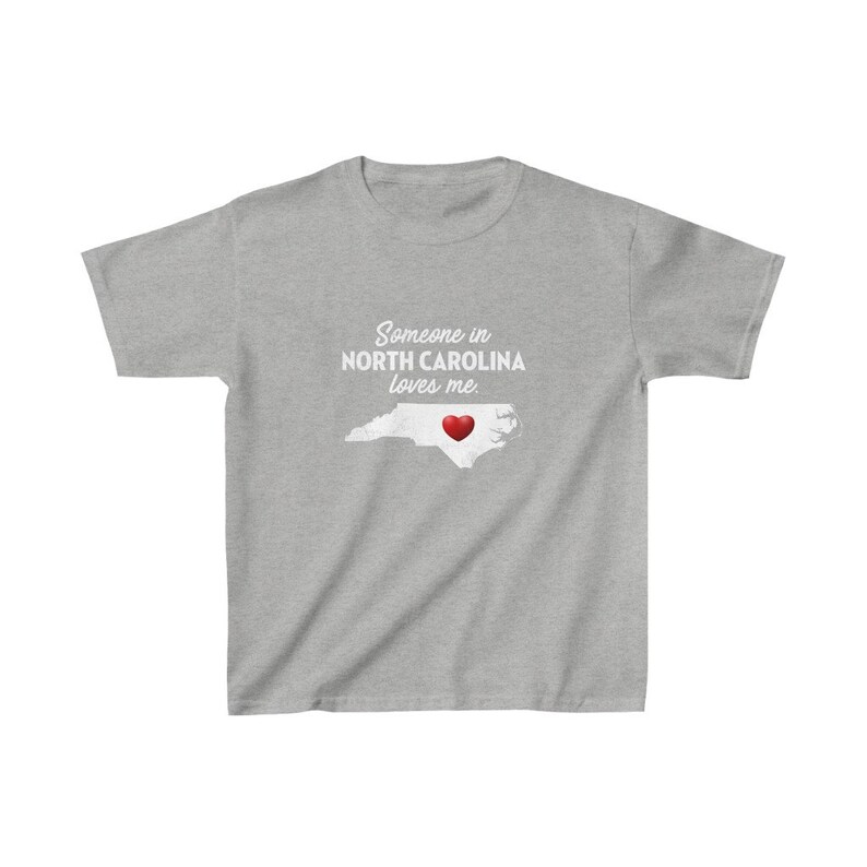 K&ouml;nnte beinhalten: Graues T-Shirt mit einer wei&szlig;en Umrandung von North Carolina und einem roten Herzen in der Mitte. Der Text "Jemand in North Carolina liebt mich" ist auf das T-Shirt gedruckt.