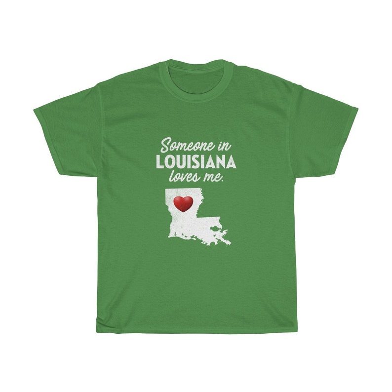 May include: Green t-shirt with white text that reads "Someone in LOUISIANA loves me."  A white outline of the state of Louisiana with a red heart in the center is below the text.
