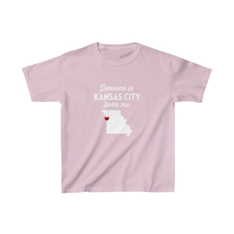 May include: Pink t-shirt with a white outline of the state of Missouri and the text "Someone in Kansas City loves me." A red heart is placed over Kansas City.