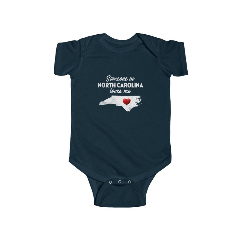 Peut inclure: Combinaison b&eacute;b&eacute; bleu marine avec un contour blanc de l'&eacute;tat de Caroline du Nord et un c&oelig;ur rouge au centre. Le texte "Someone in NORTH CAROLINA loves me." est imprim&eacute; sur la combinaison.