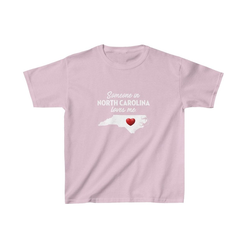 K&ouml;nnte beinhalten: Rosafarbenes T-Shirt mit einer wei&szlig;en Umrandung des Bundesstaates North Carolina und einem roten Herzen in der Mitte. Der Text "Jemand in North Carolina liebt mich." ist auf das T-Shirt gedruckt.