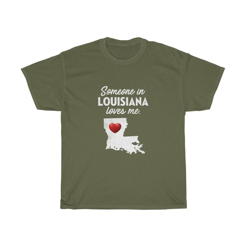 May include: Green t-shirt with white text that reads "Someone in Louisiana loves me."  A red heart is inside the outline of the state of Louisiana.