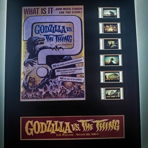 May include: A framed movie poster for the 1964 film "Godzilla vs. The Thing". The poster features a large image of Godzilla attacking a city. The poster is in color and has a black frame. The text on the poster reads "What is it... how much terror can you stand?" and "Godzilla vs. The Thing". The poster also includes the text "U.S. Release - August 20, 1964".