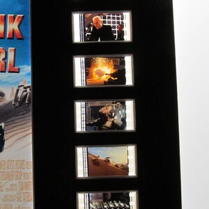 Puede incluir: Un marco negro con siete tiras de celuloide que muestran escenas de la pel&iacute;cula "Tank Girl". Las celdas de pel&iacute;cula est&aacute;n dispuestas verticalmente. Las celdas de pel&iacute;cula muestran a una mujer con cabello blanco, un hombre con traje, una explosi&oacute;n, un hombre en un desierto, una escena del desierto y un primer plano de un brazo mec&aacute;nico.