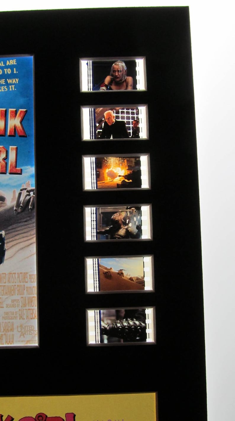 Puede incluir: Un marco negro con siete tiras de celuloide que muestran escenas de la pel&iacute;cula "Tank Girl". Las celdas de pel&iacute;cula est&aacute;n dispuestas verticalmente. Las celdas de pel&iacute;cula muestran a una mujer con cabello blanco, un hombre con traje, una explosi&oacute;n, un hombre en un desierto, una escena del desierto y un primer plano de un brazo mec&aacute;nico.