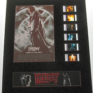 May include: A framed movie poster for the film "Hellboy: Here to Protect". The poster features a red-skinned demon with horns and a large gun. The poster is surrounded by a black frame and includes several film strips from the movie.