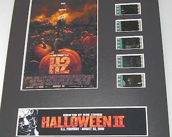 Peut inclure: Une affiche de film encadrée pour le film "Halloween II", réalisé par Rob Zombie. L'affiche présente une citrouille avec le titre du film et la date de sortie. L'affiche est entourée de bandes de film du film.