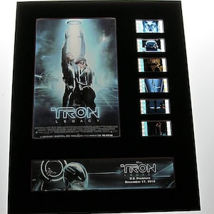 May include: Framed Tron Legacy movie poster with film stills. The poster features two figures in black suits with glowing lines, and the title "TRON LEGACY". Below, a banner reads "U.S. Premiere December 17, 2010".
