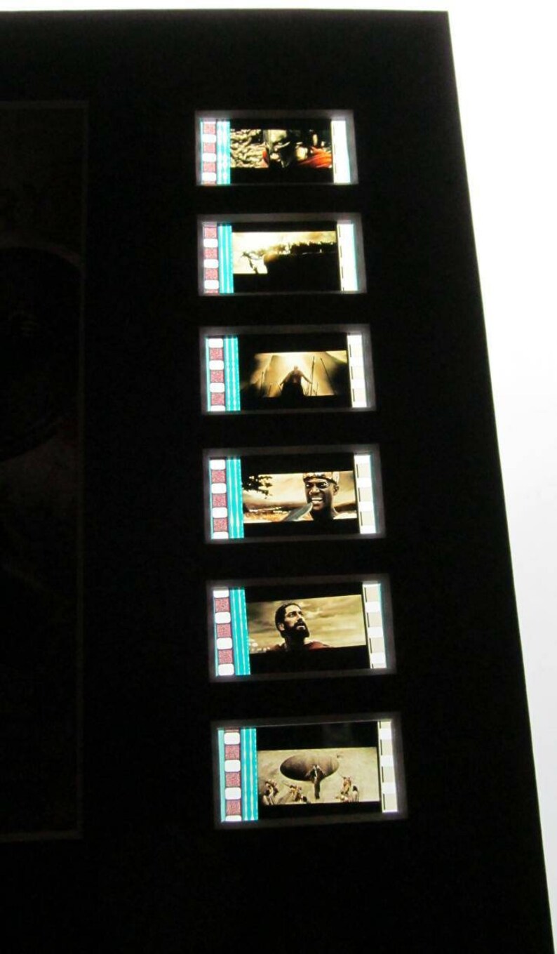 May include: A framed set of film strips with scenes from a movie. The film strips are black and white with a blue border. The scenes show a man in a dark suit, a man in a white shirt, and a man in a dark shirt.