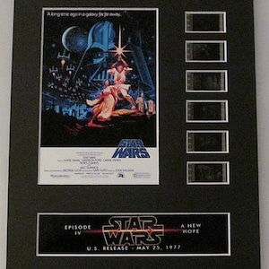 May include: A framed movie poster for Star Wars: Episode IV - A New Hope. The poster features a black and white image of Darth Vader, Luke Skywalker, and Princess Leia. The poster is surrounded by a black frame and includes five film strips.