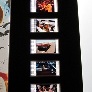 May include: A set of film strips featuring scenes from a movie. The strips are framed and displayed on a black background. The scenes include a man in a hat, a car driving down a road, and a group of people.