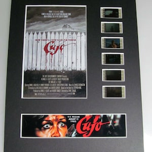 May include: A movie poster for the film "Cujo" featuring a white picket fence with red blood splatters and the title "Cujo" in red. The poster also includes a smaller image of a woman's face with wide, terrified eyes. The text "U.S. Release August 12, 1983" is also visible.