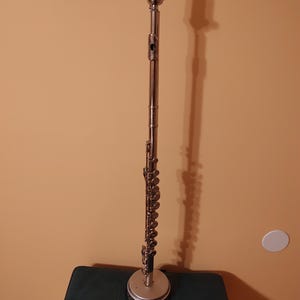 May include: A silver flute lamp with a silver light fixture on top. The lamp is sitting on a dark green table.