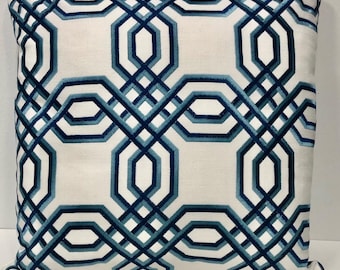 May include: Square throw pillow with a geometric design. The pillow features a white background with a repeating pattern of interlocking blue and teal shapes. The design is embroidered on the fabric.