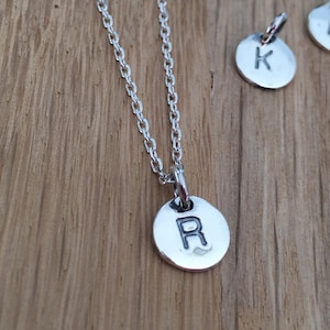Może przedstawiać: Srebrny łańcuszek z srebrnym wisiorkiem z literą "R" w prostym, nowoczesnym kroju.