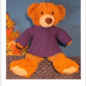 May include: A plush teddy bear with golden-brown fur and a cream-colored muzzle wearing a purple knitted sweater with a broken rib texture. The text "Broken Rib Bear Sweater Pattern" is displayed above the bear.