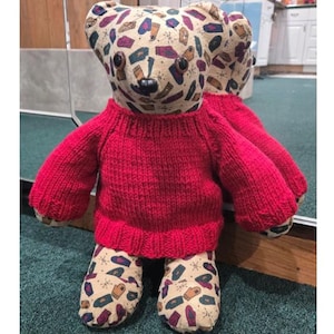 Könnte beinhalten: Ein Stoffbär mit einem cremefarbenen Stoffkörper, der mit einem sich wiederholenden Muster aus bunten Fäustlingen und Sternen bedruckt ist. Der Bär trägt einen leuchtend roten Strickpullover mit geripptem Ausschnitt und Bündchen. Der Text Stockinette Bear Sweater Pattern ist sichtbar.