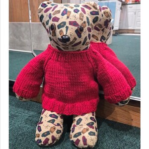 May include: A handmade bear doll wearing a bright red knitted sweater. The bear's head and feet are patterned with mittens, gloves, and other winter-themed designs. The text "Basic Bear Sweater Pattern" is at the top.