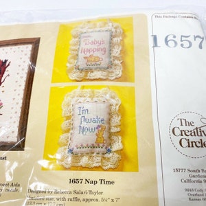 May include: A cross-stitch kit for a baby's nap time door hanger. The kit includes two designs: "Shh... Baby's Napping" and "I'm Awake Now". The finished size of the door hanger is approximately 5 1/2 inches by 7 inches.
