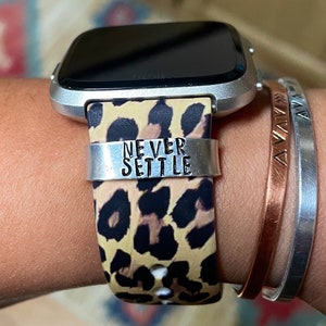 May include: A silver smartwatch with a leopard print band and a silver band that says "NEVER SETTLE".