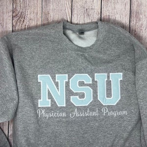 May include: Gray sweatshirt with the text "NSU Physician Assistant Program" in white and a light blue "NSU" logo.