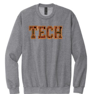 Pode incluir: Uma camisa de moletom cinza com a palavra "TECH" impressa na frente em letras laranja. As letras são compostas por um padrão de placa de circuito.
