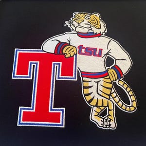 May include: Embroidered patch featuring a tiger mascot leaning on a large red letter "T". The tiger is wearing a white sweater with "tsu" in blue letters. The background is black.