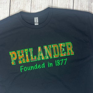 Pode incluir: Camiseta preta com texto verde que diz "Philander Founded in 1877". A palavra "Philander" está em uma fonte com um padrão colorido.