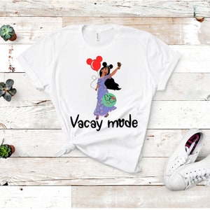May include: White t-shirt with a cartoon image of a woman with long black hair holding a red balloon and a Mickey Mouse ear headband. The text "Vacay mode" is printed in black below the image.