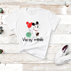 May include: White t-shirt with a cartoon Dalmatian dog wearing Mickey Mouse ears and holding a balloon. The dog is wearing a red bow and has a black nose. The text "Vacay mode" is printed below the dog.