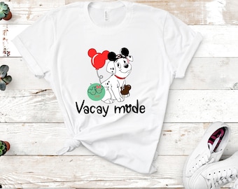 May include: White t-shirt with a cartoon Dalmatian dog wearing Mickey Mouse ears and holding a balloon. The dog is wearing a red bow and has a black nose. The text "Vacay mode" is printed below the dog.