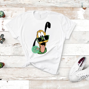 May include: White t-shirt with a cartoon image of a dog wearing sunglasses. The dog is yellow with black ears and a green collar. The dog is sticking its tongue out. The text "Goofy" is in a red circle with white Mickey Mouse ears.