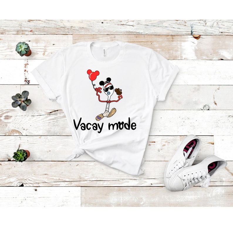 May include: White t-shirt with a cartoon image of a toy spoon wearing sunglasses and a Mickey Mouse hat, holding a balloon and a toy. The text "Vacay mode" is printed below the image.