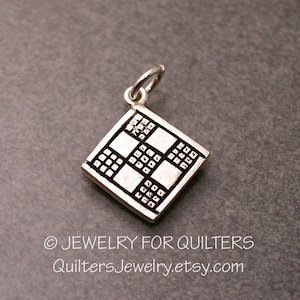May include: Silver charm in the shape of a quilt block with a checkerboard pattern. The charm is designed for quilters and features a small loop for attaching to a necklace or bracelet.