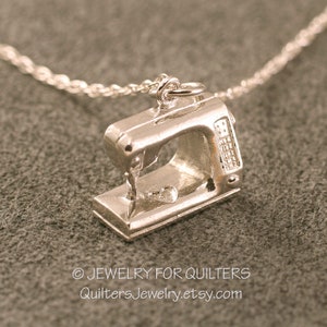 May include: Silver sewing machine charm necklace. The charm is a detailed miniature of a sewing machine with a small heart on the base. The necklace is on a silver chain.