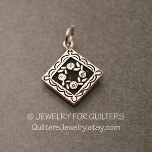 May include: Silver charm with a square design featuring a floral pattern. The charm is designed for quilters and features a floral motif.
