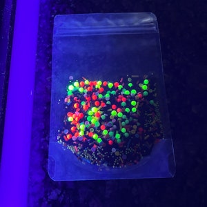 May include: A clear plastic bag filled with colourful sprinkles. The sprinkles are a mix of red, green, yellow, and black. The sprinkles are in a variety of shapes and sizes.
