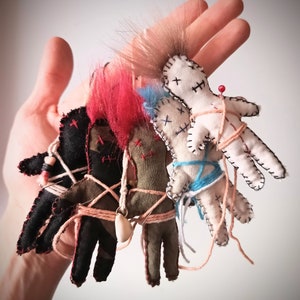 Puede incluir: Cuatro muñecas vudú hechas a mano con diferentes telas y lana atadas alrededor de ellas. Las muñecas están atadas juntas con cuerda y tienen alfileres clavados en ellas.