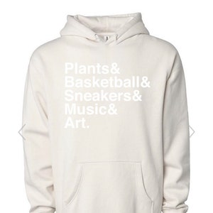 May include: A cream-coloured hoodie with a white graphic that reads "Plants & Basketball & Sneakers & Music & Art."