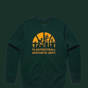 Puede incluir: Una sudadera de color verde oscuro con un gráfico amarillo de un aro de baloncesto con plantas en su interior. El texto "Plantsketball Aesthetic Dept." está impreso debajo del gráfico.