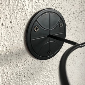 May include: Black basketball-shaped wall mount with three screws. The mount has a metal hook extending out from the center.
